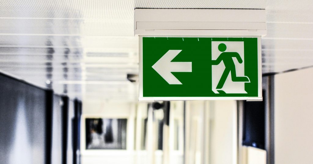 pexels-photo-134065-134065 Green emergency exit sign with directional arrow in a hallway.